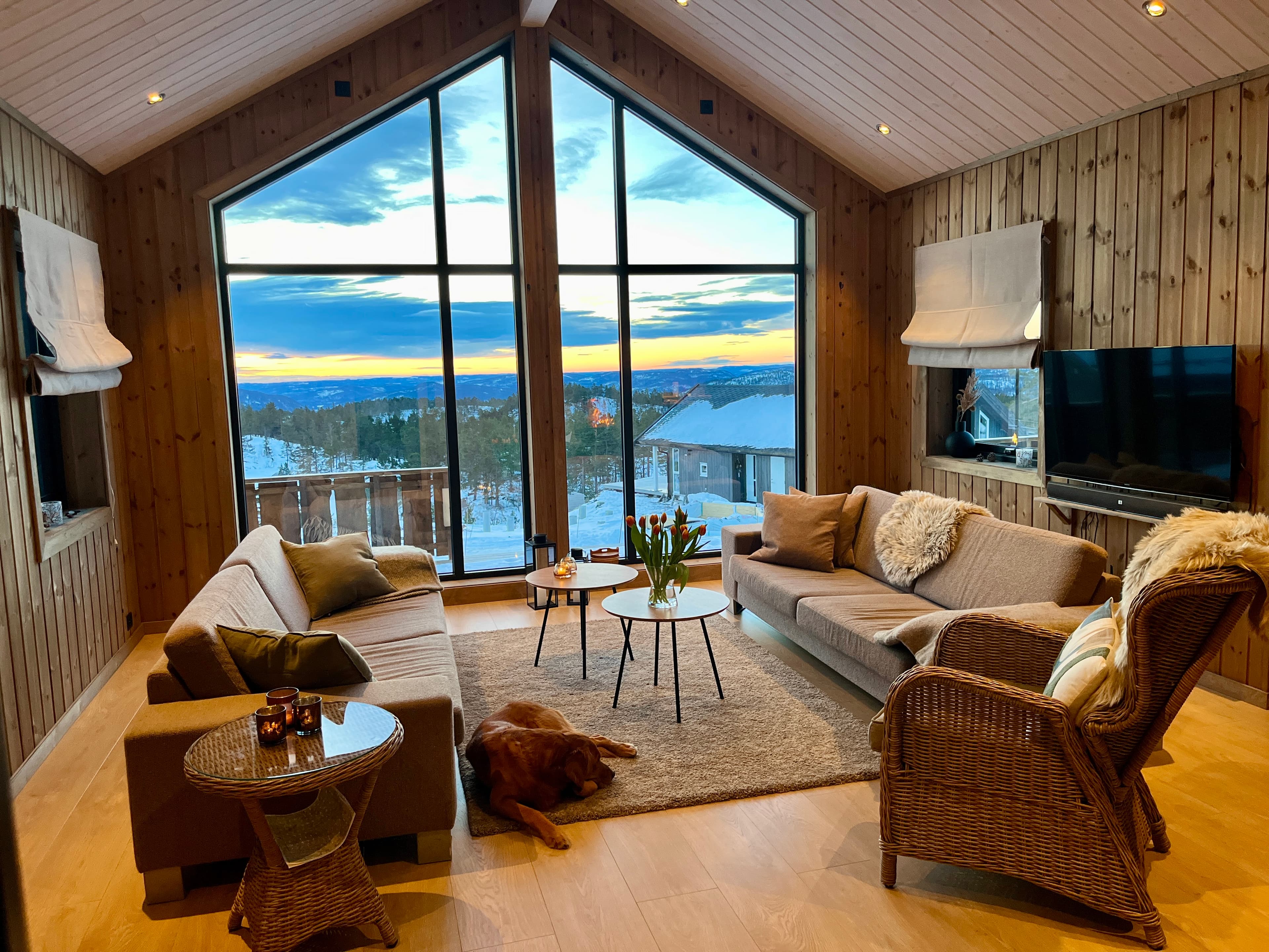 Stue med panoramavindu og utsikt mot solnedgang over fjellet